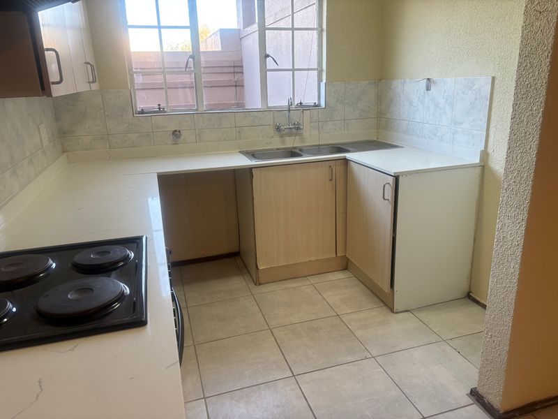A functional kitchen featuring built-in cabinetry, a double basin sink, and an electric hob, with tiled flooring and splashbacks throughout.