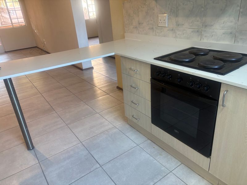 A clean, functional kitchen featuring light wood cabinetry, stone countertops, a built-in oven with electric hob, and a convenient breakfast bar extension.