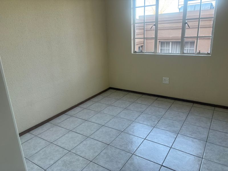An empty bedroom featuring neutral tiled flooring and a steel-framed window, providing a blank canvas for personalization.