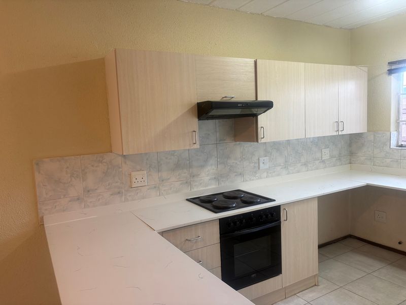 A functional kitchen featuring light wood-finish cabinetry, stone-look countertops, a built-in oven with hob, and a tiled backsplash.