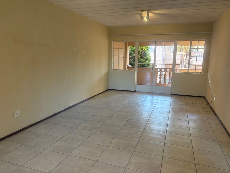 An empty living room featuring tiled flooring and a sliding glass door leading to an outdoor balcony area.