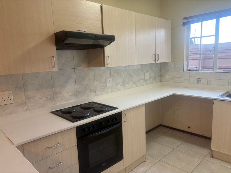 A functional kitchen featuring light wood-finish cabinetry, white laminate countertops, a built-in oven with hob, and tiled flooring.