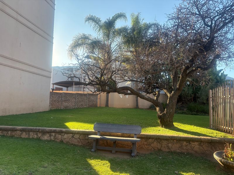 A communal garden area featuring a lawn, mature tree, and low stone-clad retaining wall with brick boundary fencing.