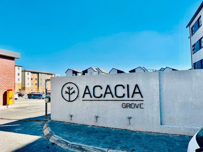 Entrance view of Acacia Grove apartment complex featuring a prominent boundary wall with signage and paved driveway access.