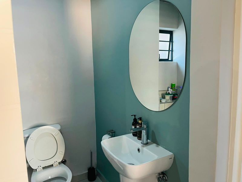 A clean and modern bathroom featuring a pedestal basin with a chrome mixer tap, an oval wall mirror, and a standard toilet.