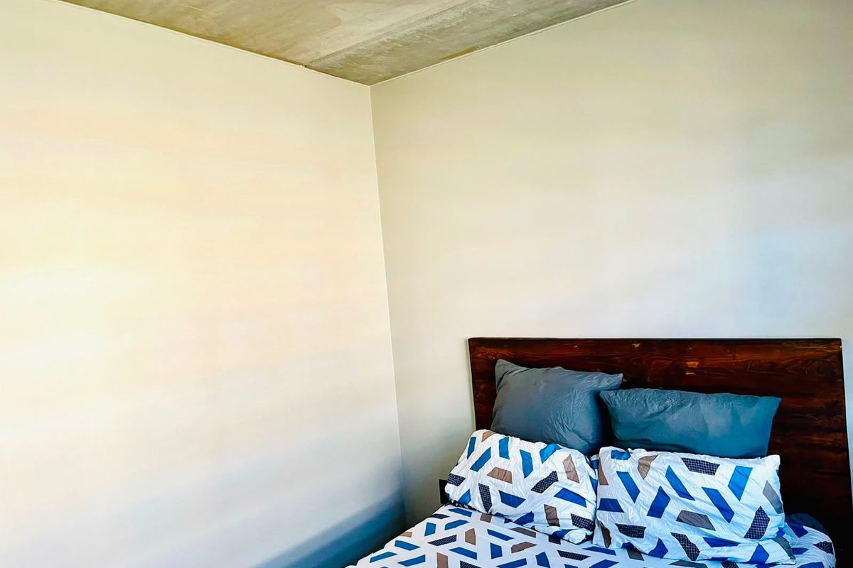 A bedroom featuring a minimalist aesthetic with an exposed concrete ceiling and plain painted walls.