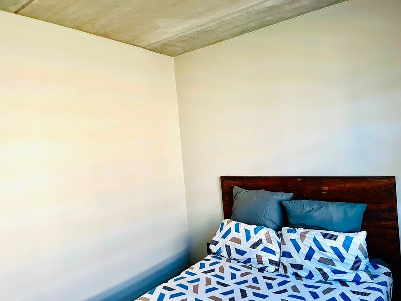 A bedroom featuring a minimalist aesthetic with an exposed concrete ceiling and plain painted walls.