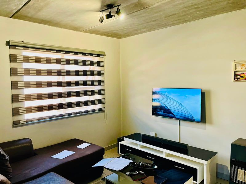 A living room featuring an exposed concrete ceiling, track lighting, and modern roller blinds, providing a contemporary industrial aesthetic.