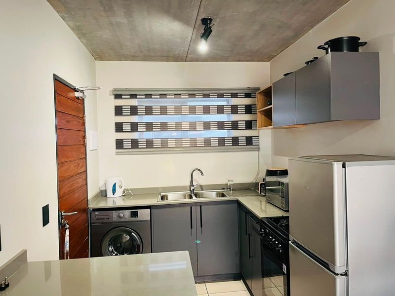 Modern kitchen featuring grey cabinetry, stone countertops, stainless steel sink, built-in oven, and an exposed concrete ceiling, providing a contemporary industrial aesthetic.