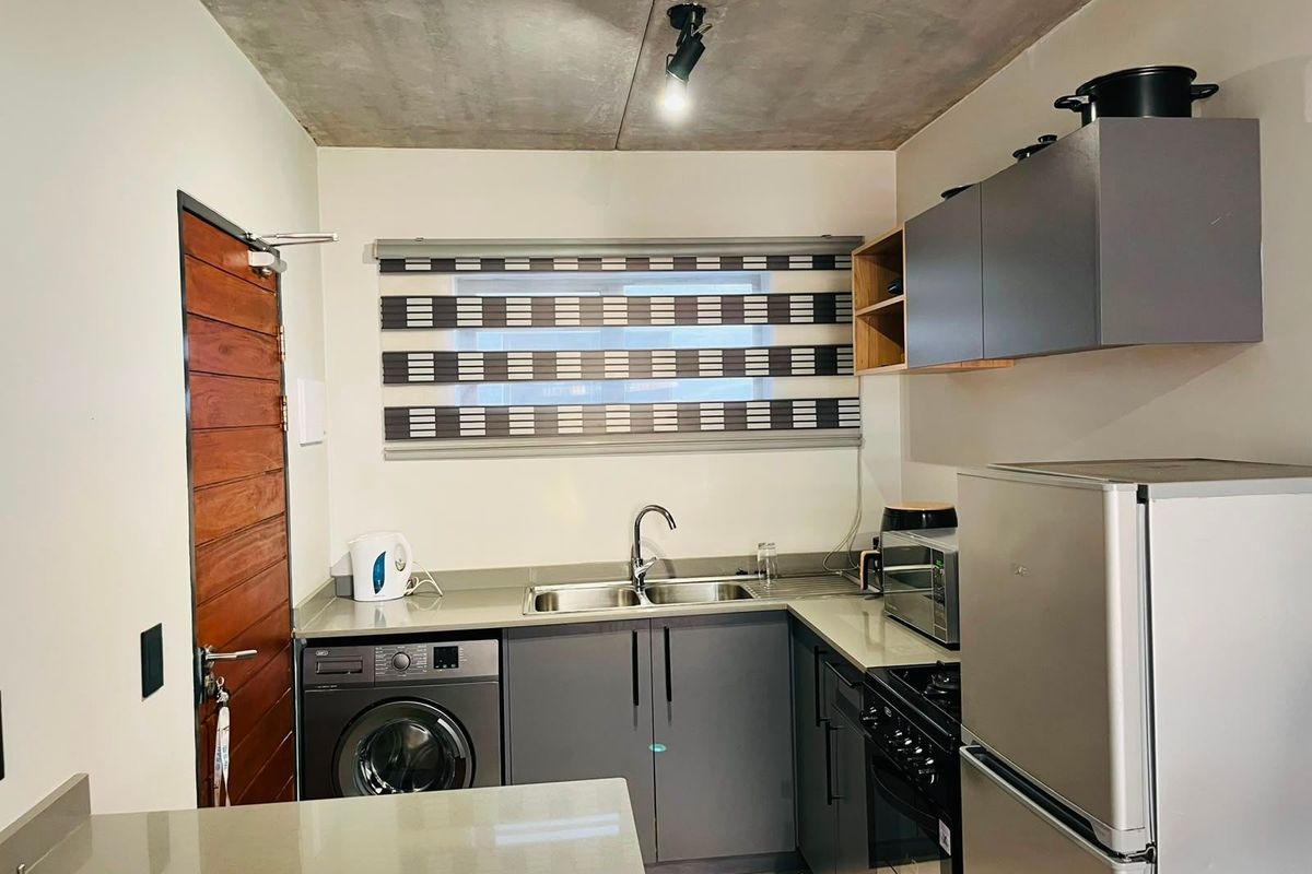 Modern kitchen featuring grey cabinetry, stone countertops, stainless steel sink, built-in oven, and an exposed concrete ceiling, providing a contemporary industrial aesthetic.