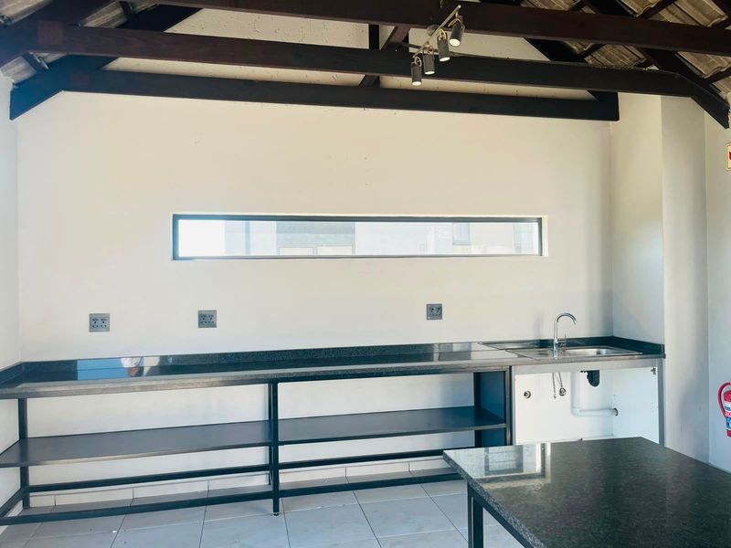 A functional kitchen area featuring granite countertops, a stainless steel sink, exposed timber beams, and tiled flooring in a clean, open-plan layout.