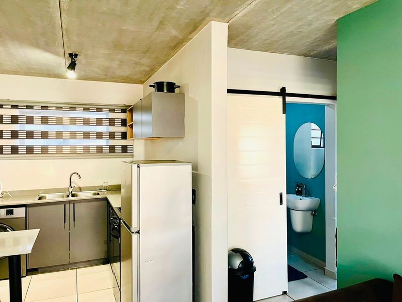 Open-plan kitchen featuring grey cabinetry and exposed concrete ceilings, with an adjacent bathroom accessed via a sliding barn door.