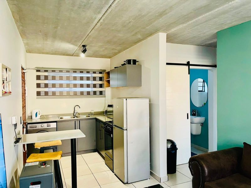 Open-plan kitchen featuring modern grey cabinetry, stainless steel appliances, and an exposed concrete ceiling, with an adjacent bathroom accessible via a sliding barn door.