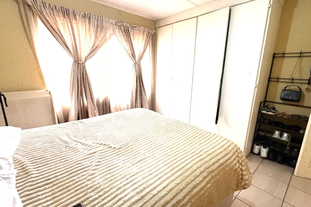 A bedroom featuring built-in cupboards and tiled flooring, requiring cosmetic updates to the wall and ceiling finishes.