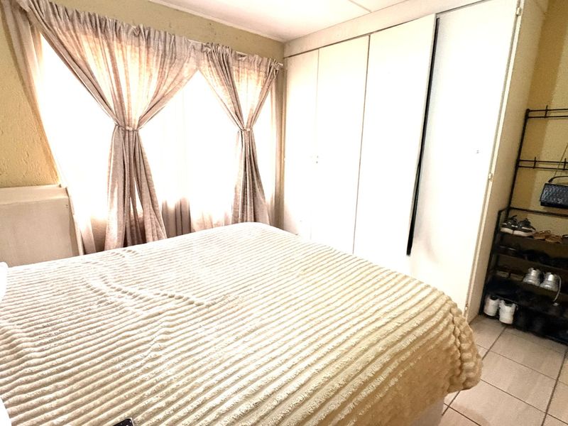 A bedroom featuring built-in cupboards and tiled flooring, requiring cosmetic updates to the wall and ceiling finishes.