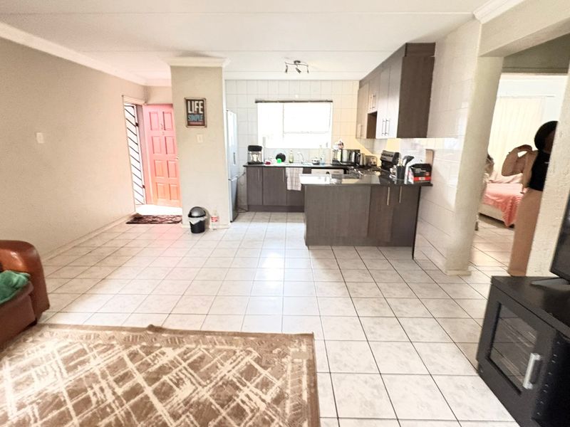 Open-plan living area featuring tiled flooring and a functional kitchen with built-in cabinetry and a peninsula, providing a versatile space for daily living.