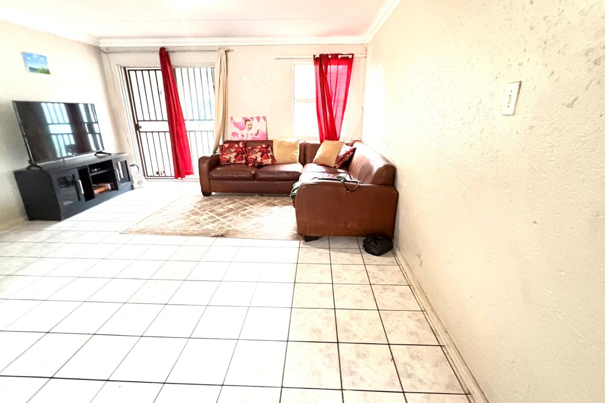 A living room area featuring tiled flooring and a sliding door with a security gate, providing access to the exterior.