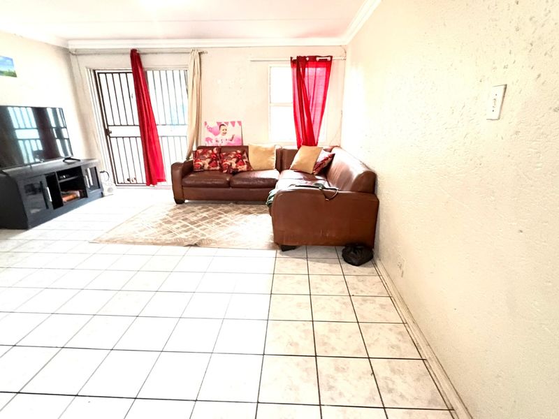 A living room area featuring tiled flooring and a sliding door with a security gate, providing access to the exterior.