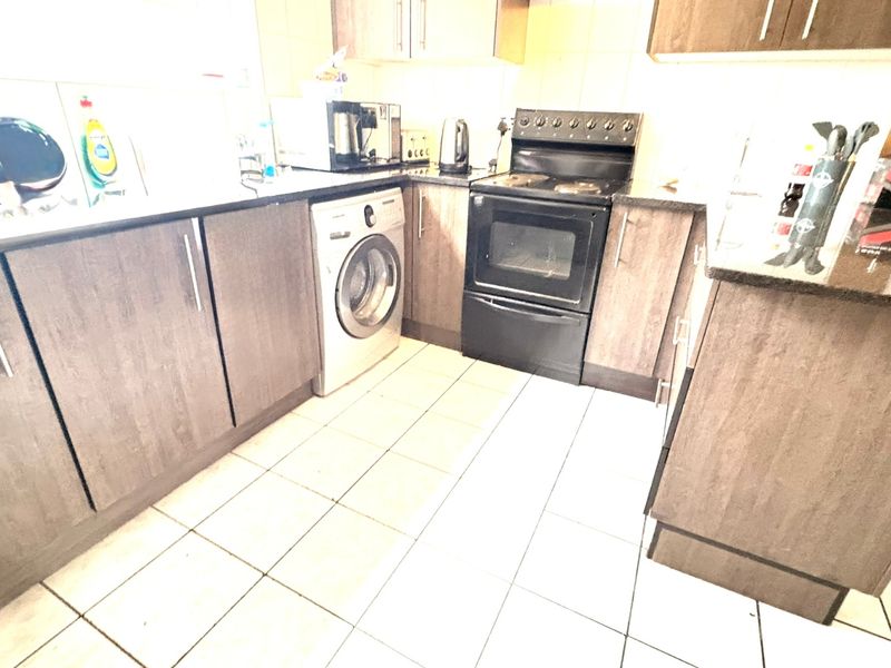 A functional kitchen featuring dark wood-look cabinetry, granite countertops, tiled flooring, and a built-in oven with an electric hob.