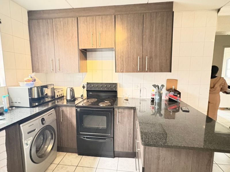 A functional kitchen featuring wood-finish cabinetry, granite countertops, a tiled backsplash, and a built-in electric stove with an integrated washing machine.
