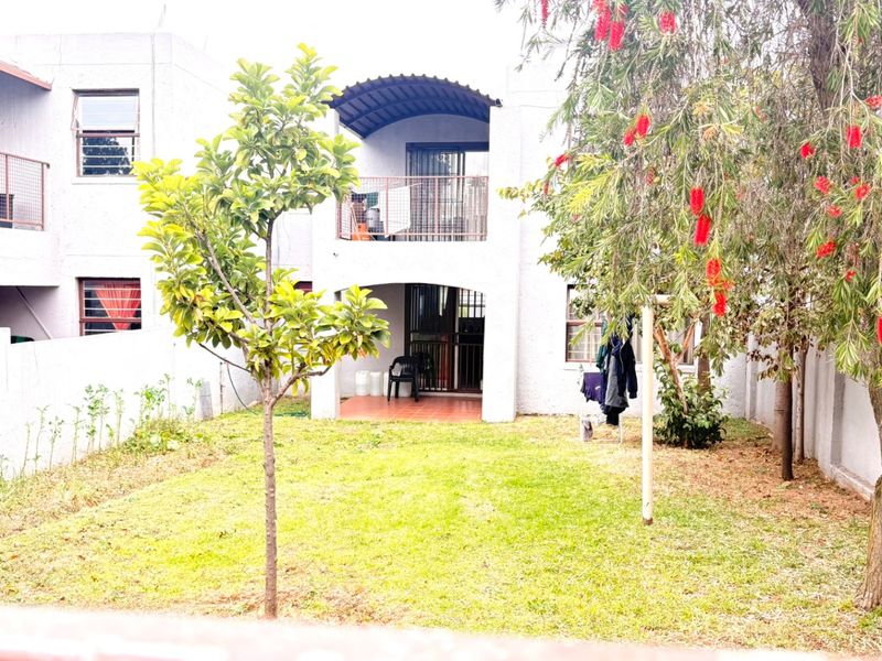 Rear view of the apartment building featuring a ground floor patio, upper level balcony, and a private garden area.