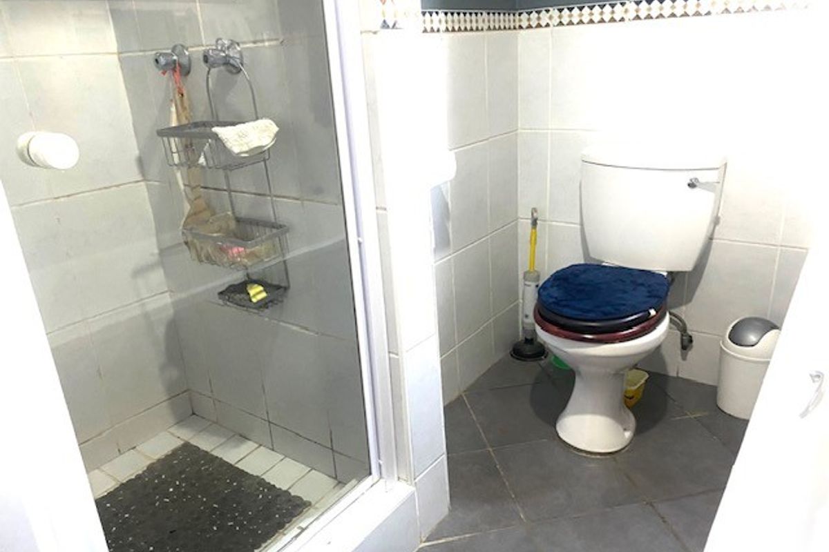 A compact bathroom featuring a shower enclosure and a standard toilet with tiled walls and flooring throughout.