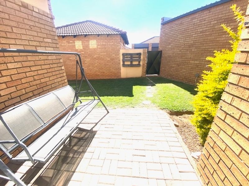 A private rear courtyard featuring brick paving, a small lawn area, and secure brick boundary walls with a metal access gate.