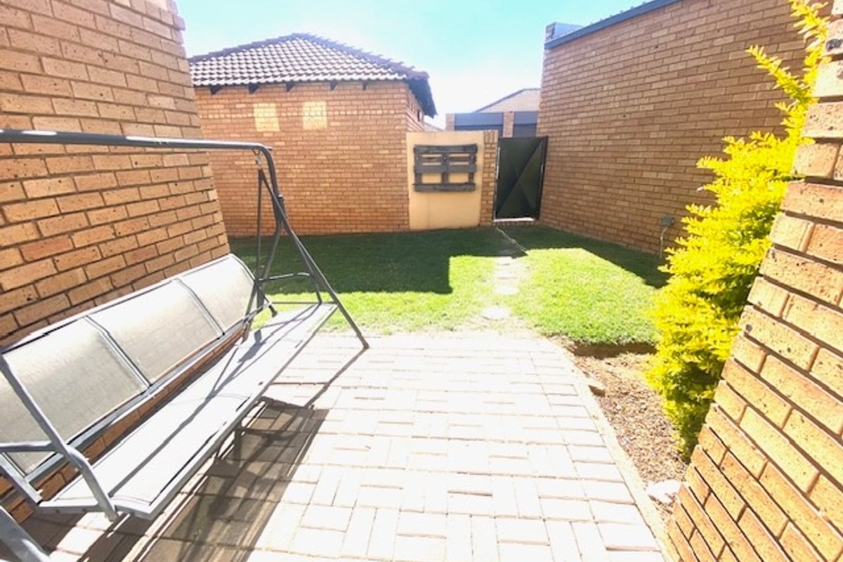 A private rear courtyard featuring brick paving, a small lawn area, and secure brick boundary walls with a metal access gate.