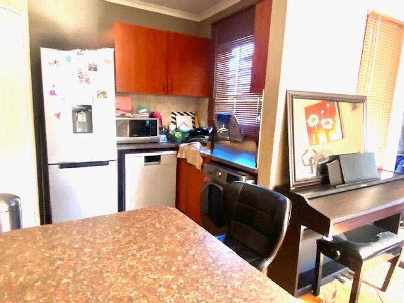 A functional kitchen area featuring laminate countertops, built-in cabinetry, and tiled flooring, with integrated space for appliances and natural light from window blinds.