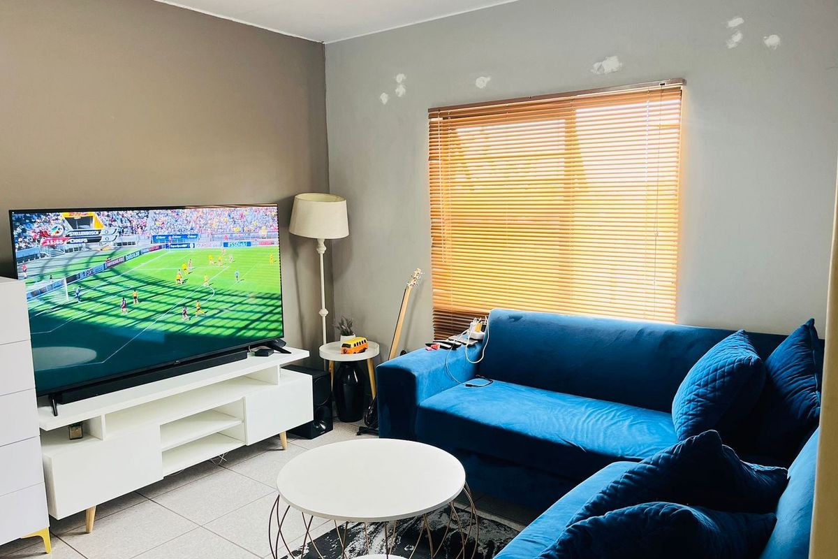 A living room featuring tiled flooring and venetian blinds, currently requiring minor wall repairs and repainting to improve the overall aesthetic.