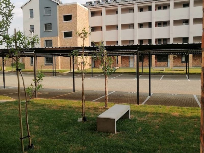 View of the apartment complex exterior featuring covered parking bays, paved driveway, and well-maintained communal lawn area with solar water heating panels on roof.