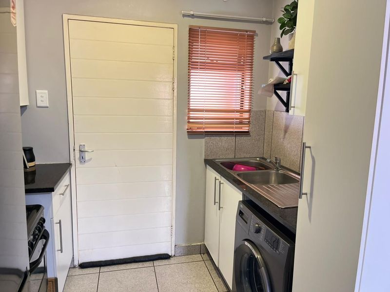 Compact kitchen featuring granite countertops, stainless steel double sink, built-in cabinetry, and tiled flooring with direct access to an exterior door.