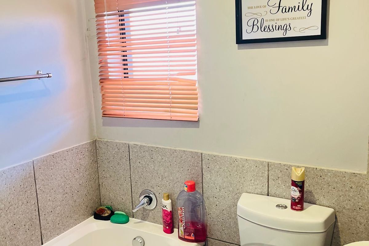 A functional bathroom featuring a bathtub, toilet, and washbasin with neutral wall tiling and a window with venetian blinds.