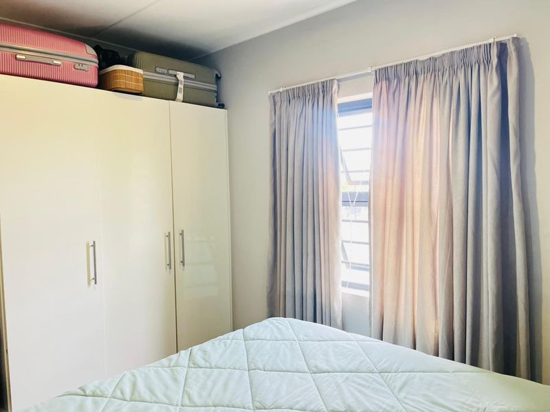 A functional bedroom featuring a white built-in wardrobe and a louvered window with neutral curtains.