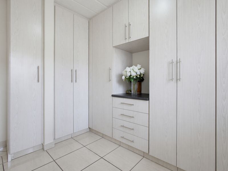 A clean and well-maintained bedroom area featuring extensive built-in cupboards with light wood-grain finish and neutral floor tiles.