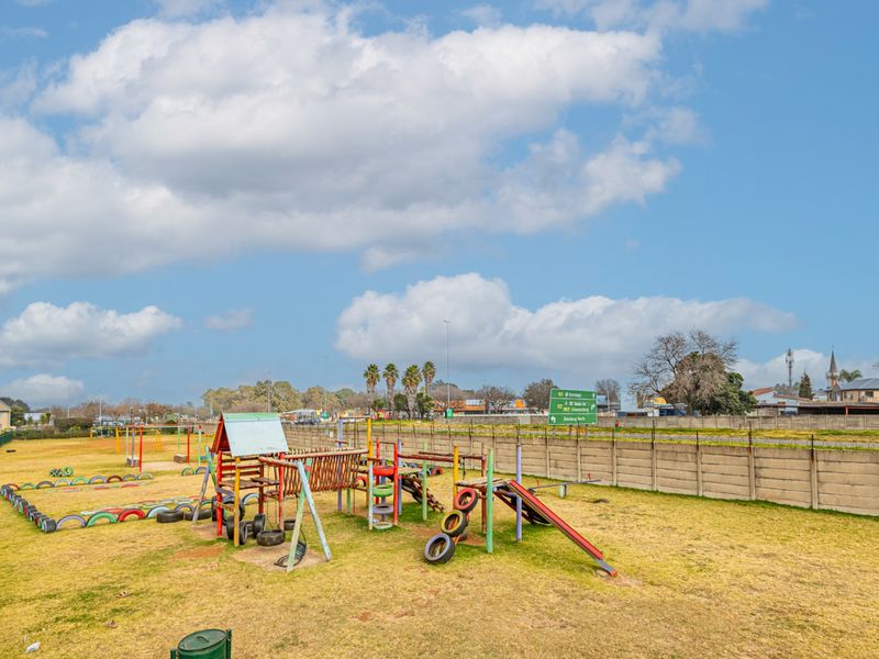 An outdoor communal area featuring a playground with fixed equipment, enclosed by a precast concrete boundary wall and security fencing.