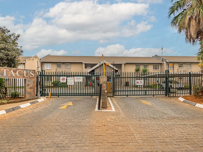 The secure entrance to the apartment complex features a gated access point, paved driveway, and perimeter security fencing.