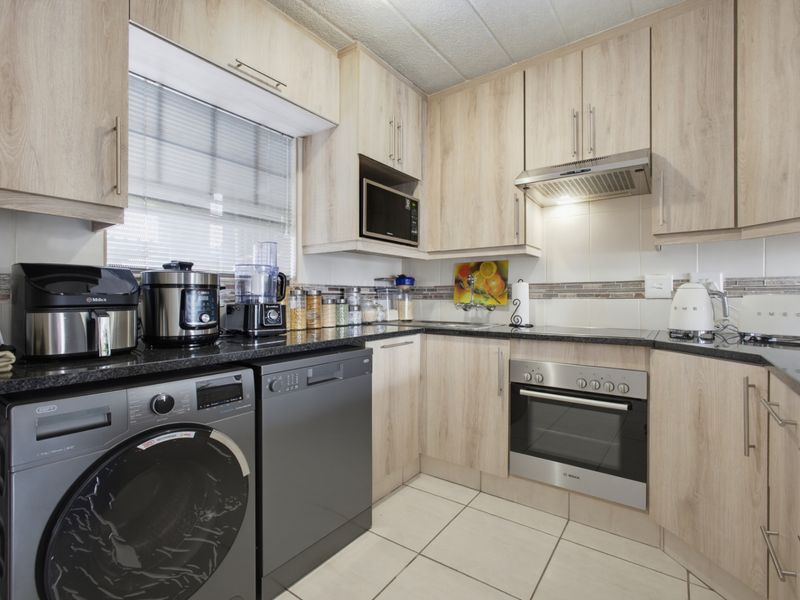 A functional kitchen featuring light wood-look cabinetry, granite countertops, tiled backsplash, and integrated appliances including an oven and extractor fan.