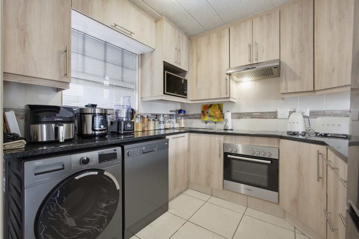 A functional kitchen featuring light wood-look cabinetry, granite countertops, tiled backsplash, and integrated appliances including an oven and extractor fan.