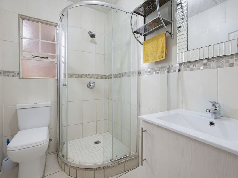 A functional bathroom featuring a curved glass shower enclosure, vanity cabinet with integrated basin, and neutral wall tiling with a decorative mosaic border.