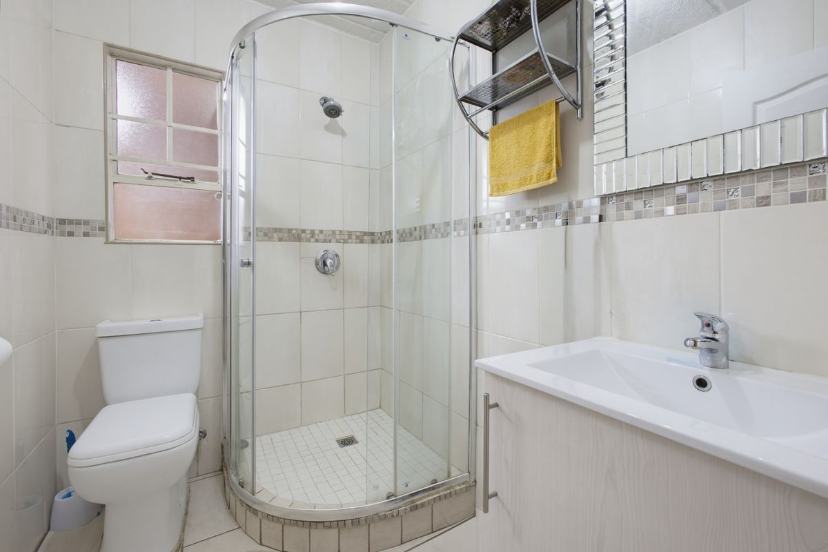 A functional bathroom featuring a curved glass shower enclosure, vanity cabinet with integrated basin, and neutral wall tiling with a decorative mosaic border.