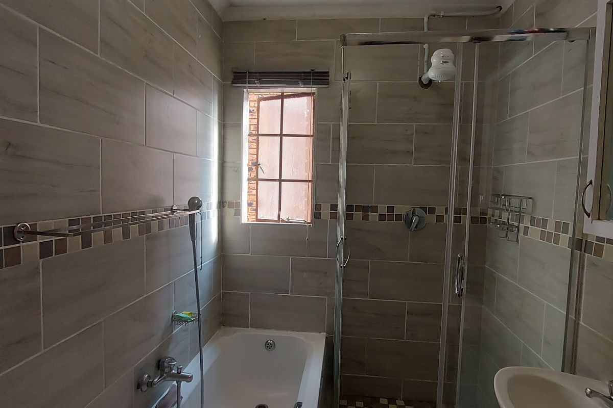 A functional bathroom featuring a built-in bathtub, separate glass shower enclosure, wall-mounted basin, and neutral tiled finishes throughout.