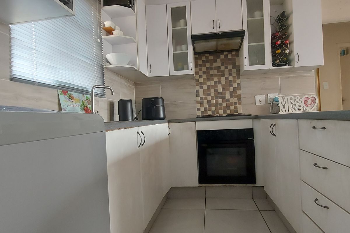 A functional kitchen featuring white cabinetry, a mosaic tile backsplash, built-in oven, extractor fan, and ceramic floor tiles.