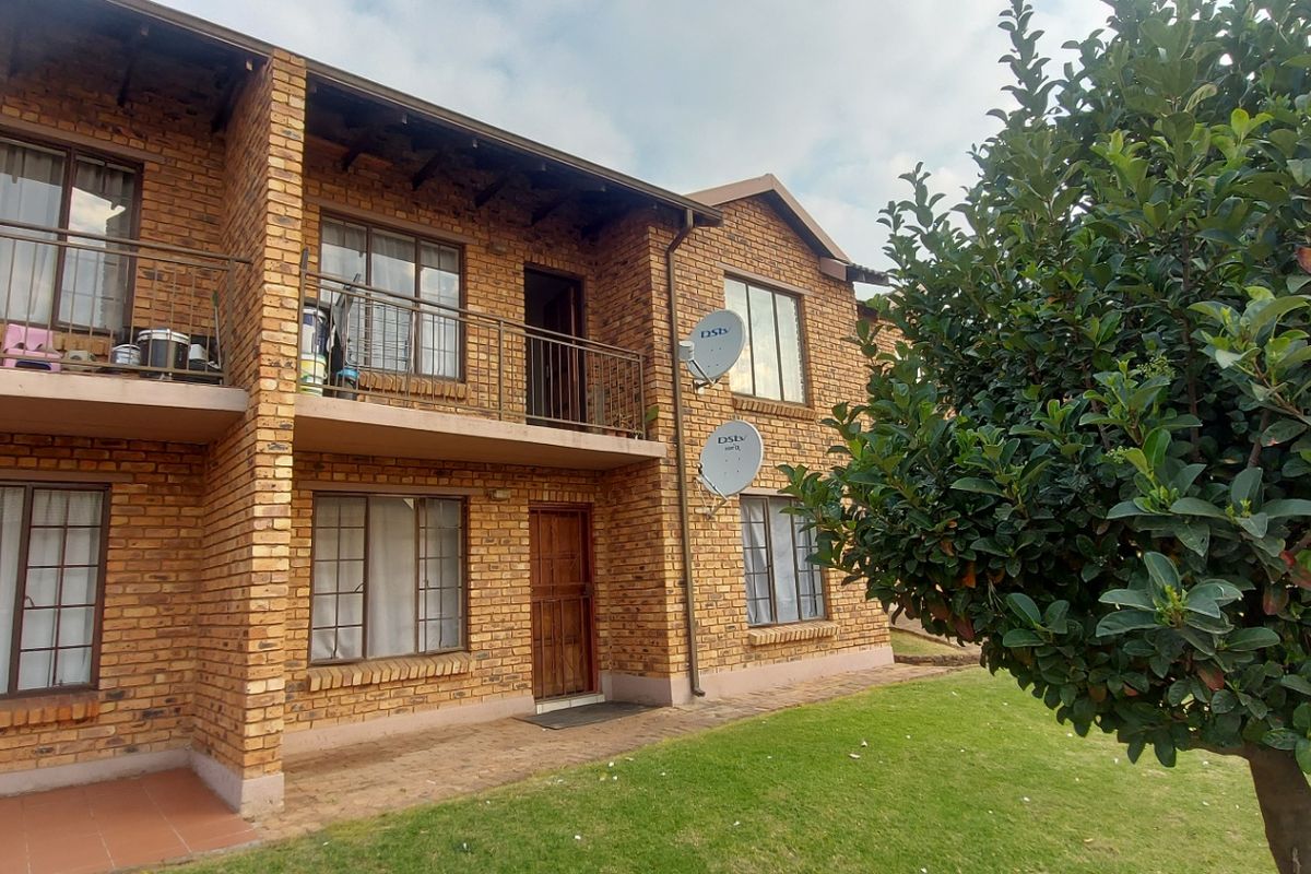 Rear view of a two-story face brick townhouse featuring a ground-floor patio and an upper-level balcony with metal railings.