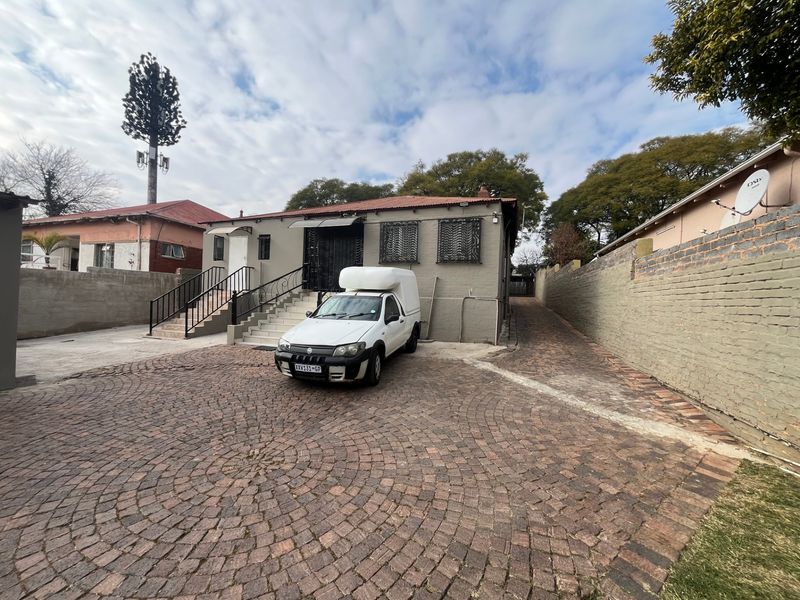 Front exterior view of the property featuring a cobblestone driveway, concrete entrance staircase with wrought iron railings, and secure brick boundary walls.