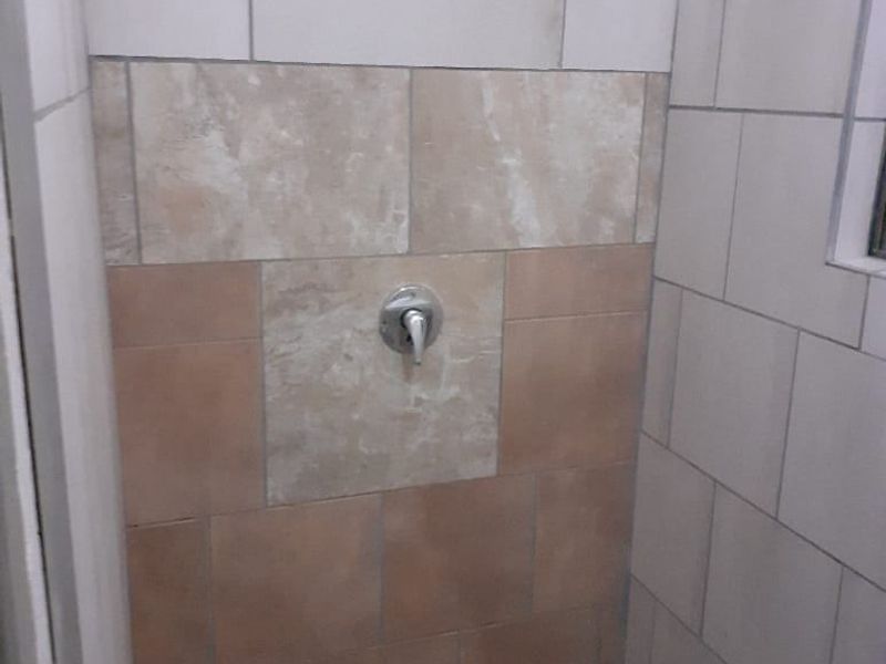 A functional shower enclosure featuring mixed-tone wall tiling and a standard shower mixer fixture.