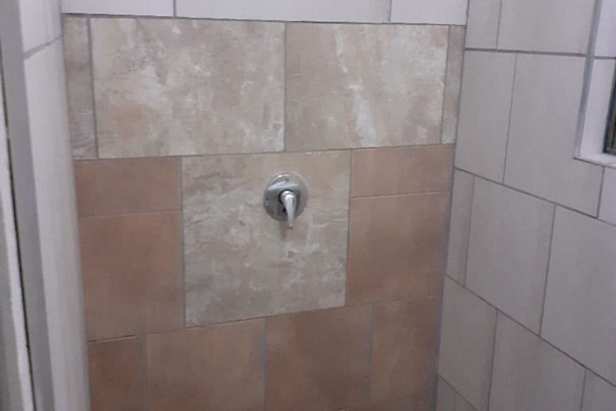 A functional shower enclosure featuring mixed-tone wall tiling and a standard shower mixer fixture.