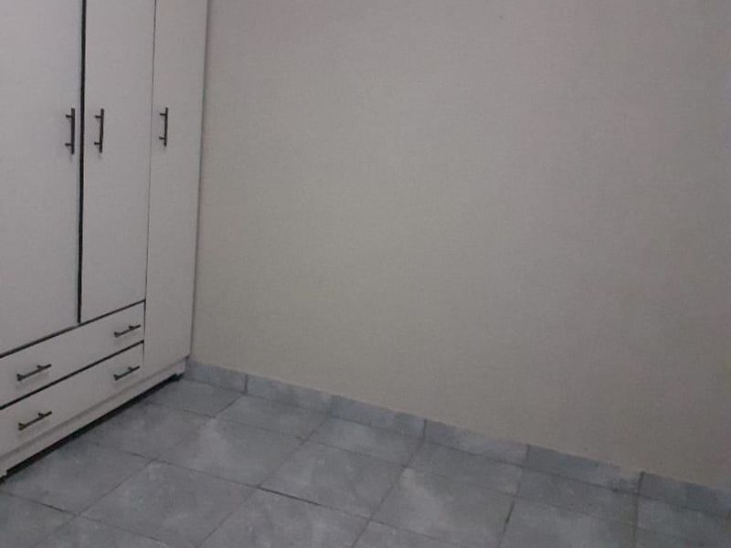 A simple, empty bedroom featuring neutral walls, tiled flooring, and a white built-in wardrobe.