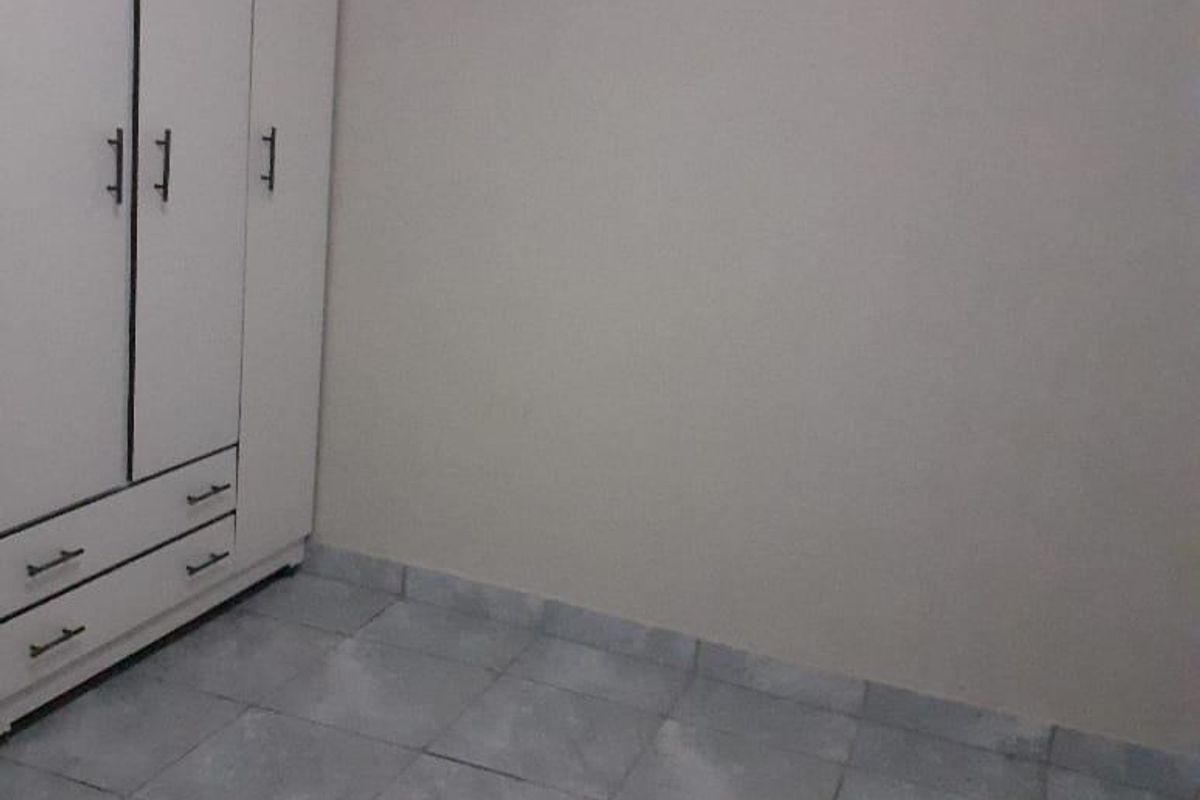 A simple, empty bedroom featuring neutral walls, tiled flooring, and a white built-in wardrobe.