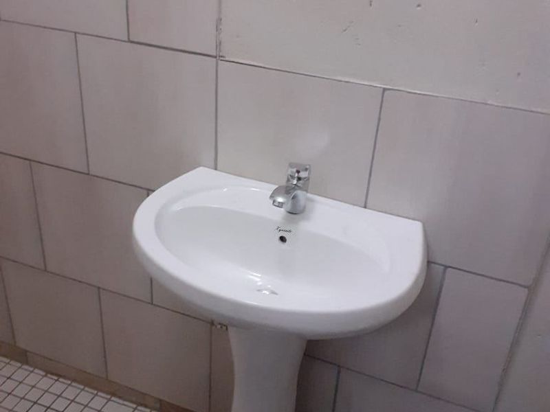 A small bathroom featuring a white pedestal basin with a chrome mixer tap, set against tiled walls and mosaic flooring in need of maintenance.